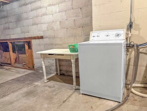 A laundry area with a washing machine and a table, a green basket, and a vent hose. - Seagulls Nest | Steps 2 Lake! Massage Chair! (Sheboygan)