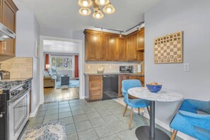 A modern kitchen with wooden cabinets, a dining area with blue chairs, and a checkered board on the wall. - Seagulls Nest | Steps 2 Lake! Massage Chair! (Sheboygan)