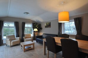 A modern living room with a dining area, large windows, and a hanging lamp. - Holiday home with 1 bedroom (Kamperland)