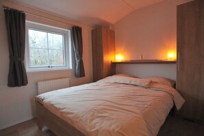 Ein Schlafzimmer mit einem Einzelbett, einem Vorhangfenster, einem Heizkörper und einem Wandregal mit einer Lampe.
