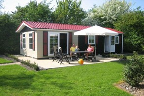 Ein kleines Haus mit rotem Dach, einer Terrasse mit Gartenmöbeln und einem großen Sonnenschirm.