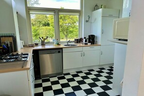 Una cocina con piso a cuadros blanco y negro, lavavajillas, estufa y ventana con vista a la vegetación.