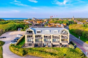 A multi-story hotel with balconies, a parking area, and a view of the sea and town. - Residence Ruimzicht 35 (Domburg)