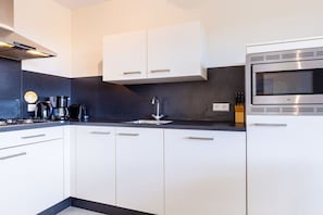 A modern kitchen with white cabinets, a stainless steel microwave, and a coffee maker. - Residence Ruimzicht 35 (Domburg)