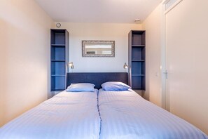 A bedroom with a double bed, two bedside tables, a mirror, and built-in shelving on either side. - Residence Ruimzicht 35 (Domburg)