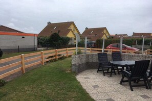 Eine Terrasse mit Außenbestuhlung und einer Steinwand, umgeben von einem Holzzaun und Häusern im Hintergrund.