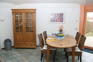Een eethoek met een houten tafel en rieten stoelen, een kast met glazen deuren en een lijstwerk met een kunstwerk aan de muur.