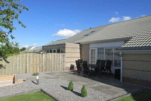 Ein Wohnhaus mit Terrasse, Außenmöbeln und einem umzäunten Garten.