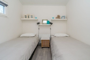 A small, clean room with two single beds, a radiator, and shelves with personal items. - Duinpark Westerschouwen - Chalet 1 (Burgh-Haamstede)