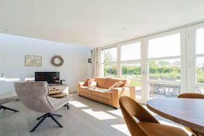 A modern living room with a sofa, a television, and a dining table. - Duinpark Westerschouwen - Chalet 1 (Burgh-Haamstede)