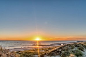 A beach with the sun setting over the horizon, creating a silhouette of the landscape. - Duinpark Westerschouwen - Chalet 1 (Burgh-Haamstede)