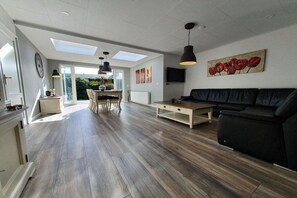 A modern living room with a black sofa, a wooden coffee table, and a dining area with a table and chairs. - Bungalow with 1 bedroom (Sint Maartenvlotbrug)