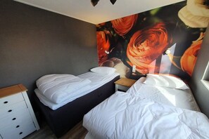 A bedroom with two beds, a nightstand, and a wall with a floral mural. - Bungalow with 1 bedroom (Sint Maartenvlotbrug)