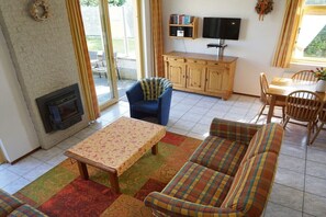 Un salon avec une cheminée, un canapé, une table et un téléviseur posé sur un meuble en bois.