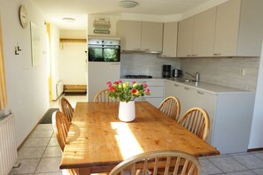 A dining area with a wooden table and chairs, a vase with flowers, and a kitchen in the background. - Holiday home with 3 bedrooms (Julianadorp aan Zee)