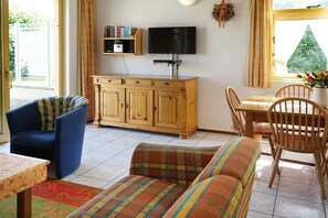 A room with a television on a stand, a wooden cabinet, a sofa, a dining table with chairs, and a window with curtains. - Holiday home with 3 bedrooms (Julianadorp aan Zee)