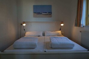 Un lit double avec deux oreillers, une tête de lit agrémentée de deux lampes murales et un tableau représentant une scène de plage au-dessus du lit.