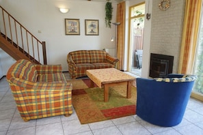 A living room with a sofa set, a coffee table, and a blue armchair. There is a staircase to the left and a fireplace to the right. - Holiday home with 3 bedrooms (Julianadorp aan Zee)