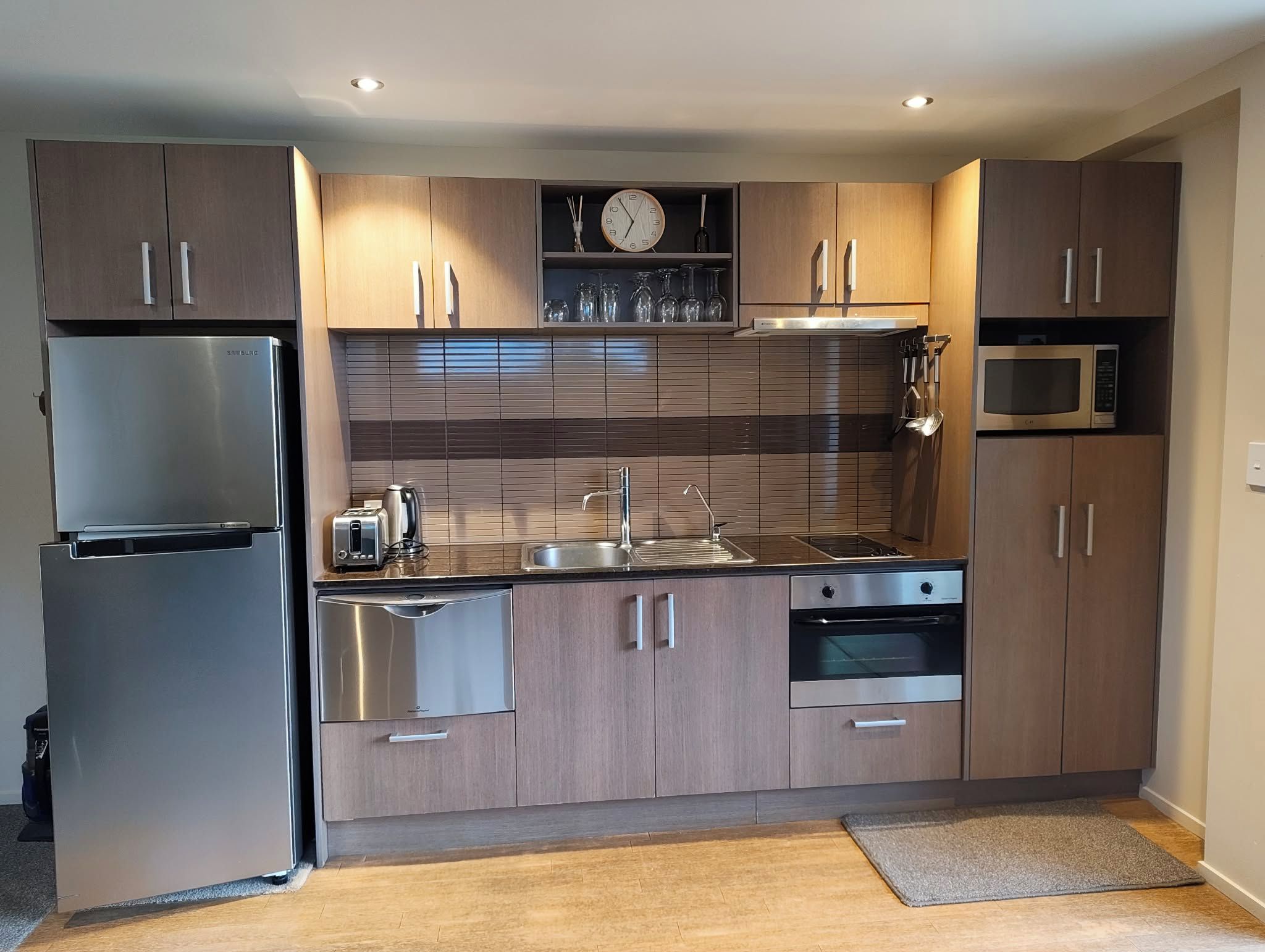 A modern kitchen with stainless steel appliances, wooden cabinets, a built-in oven, and a microwave.