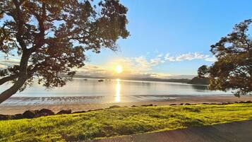 A coastal landscape with a clear sky, a body of water reflecting the sun, and a grassy area with a paved path.
