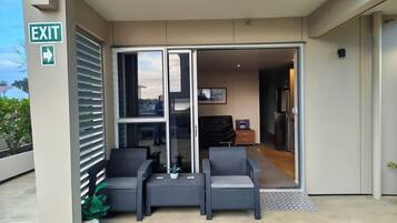 A hotel entrance with an exit sign, a glass door leading to a seating area with two chairs and a table, and a small potted plant.