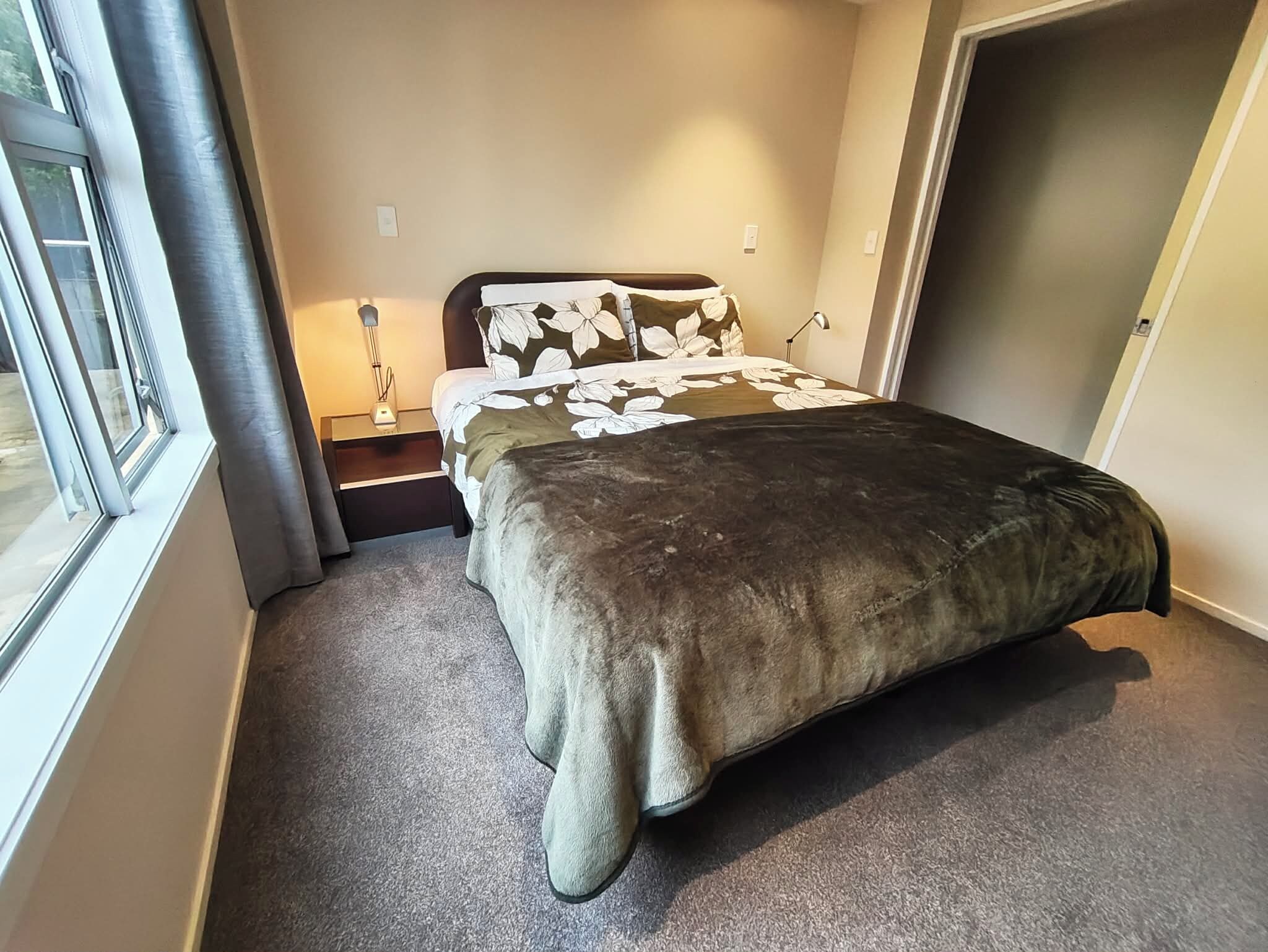 A bedroom with a bed, a nightstand, a lamp, and a window.