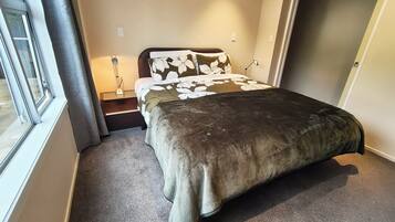 A bedroom with a bed, a nightstand, a lamp, and a window.