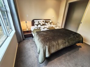 Ein Schlafzimmer mit einem Bett, einem Nachttisch, einer Lampe und einem Fenster.