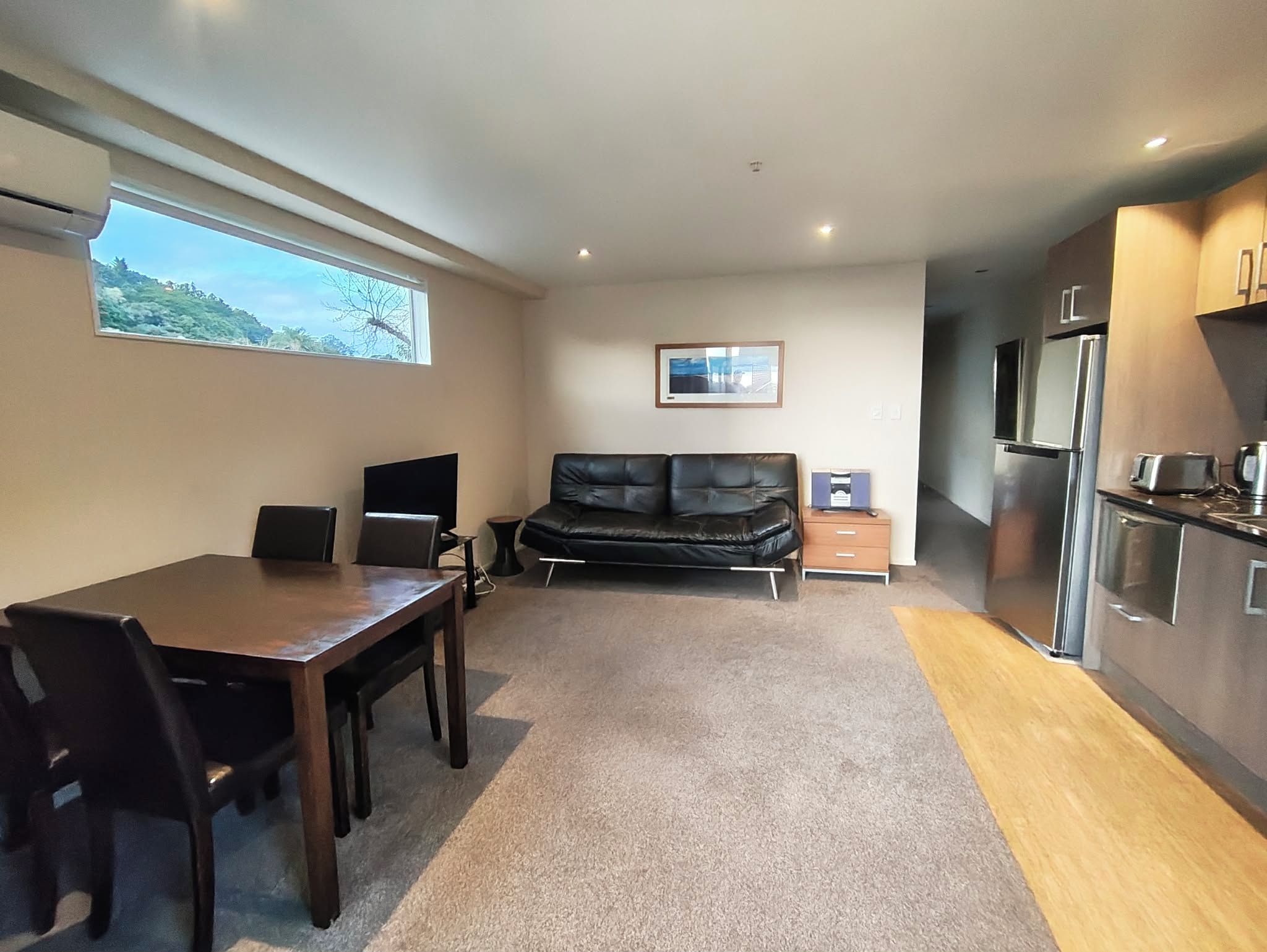 A compact living space with a dining area, sofa, kitchenette, and a window with a view.