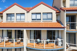 A multi-story building with a red-tiled roof, balconies with outdoor furniture, and large windows. - Breeze at Fly Point Apartment 39 (Nelson Bay)