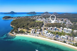 An aerial view of a coastal town with a beach, residential areas, and a large body of water. - Breeze at Fly Point Apartment 39 (Nelson Bay)