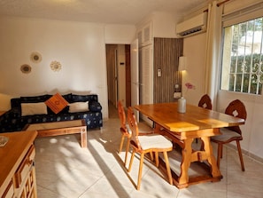 A living room with a sofa, a dining table with chairs, a bench, and a window with a view. - Don Lotario – Bungalow with communal pool (Moraira)