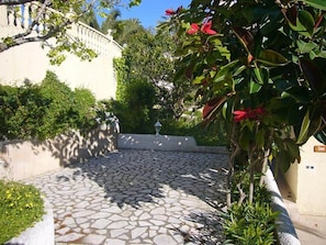 A courtyard with a stone pathway, a white wall, and a tree with red flowers. - Don Lotario – Bungalow with communal pool (Moraira)
