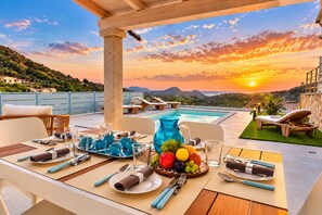 Ein Tisch ist für eine Mahlzeit gedeckt, mit Blick auf einen Pool und einen Sonnenuntergang.