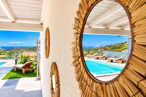 Ein Poolbereich mit Blick auf Meer und Hügel, eine Liege und ein dekorativer Spiegel.