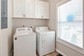 A laundry room with a washer and dryer, cabinets above, and a window with blinds. - Luxury for 2 Traveling for Business (Atlanta,)