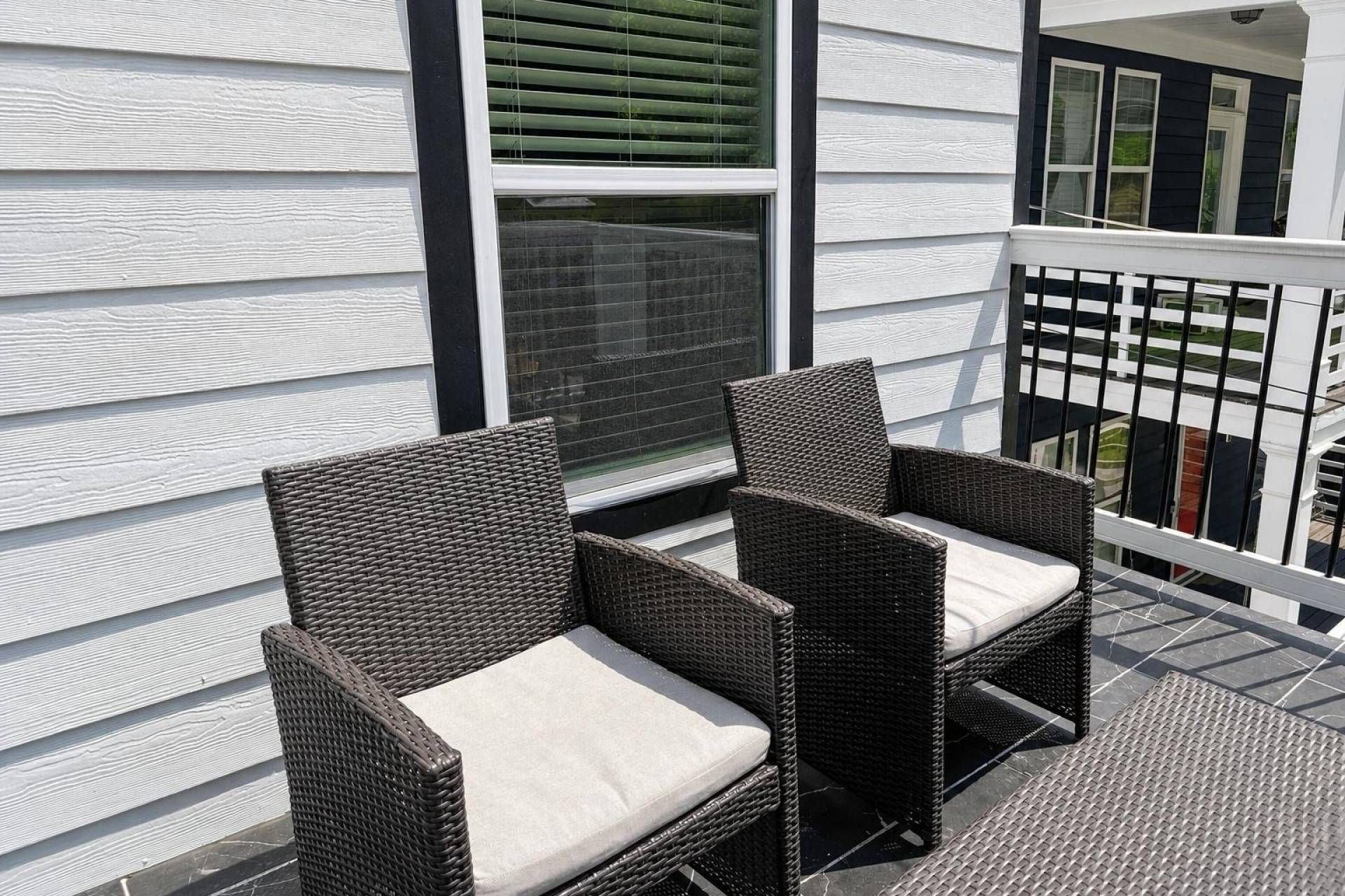 Two wicker chairs with cushions on a balcony with a white railing.