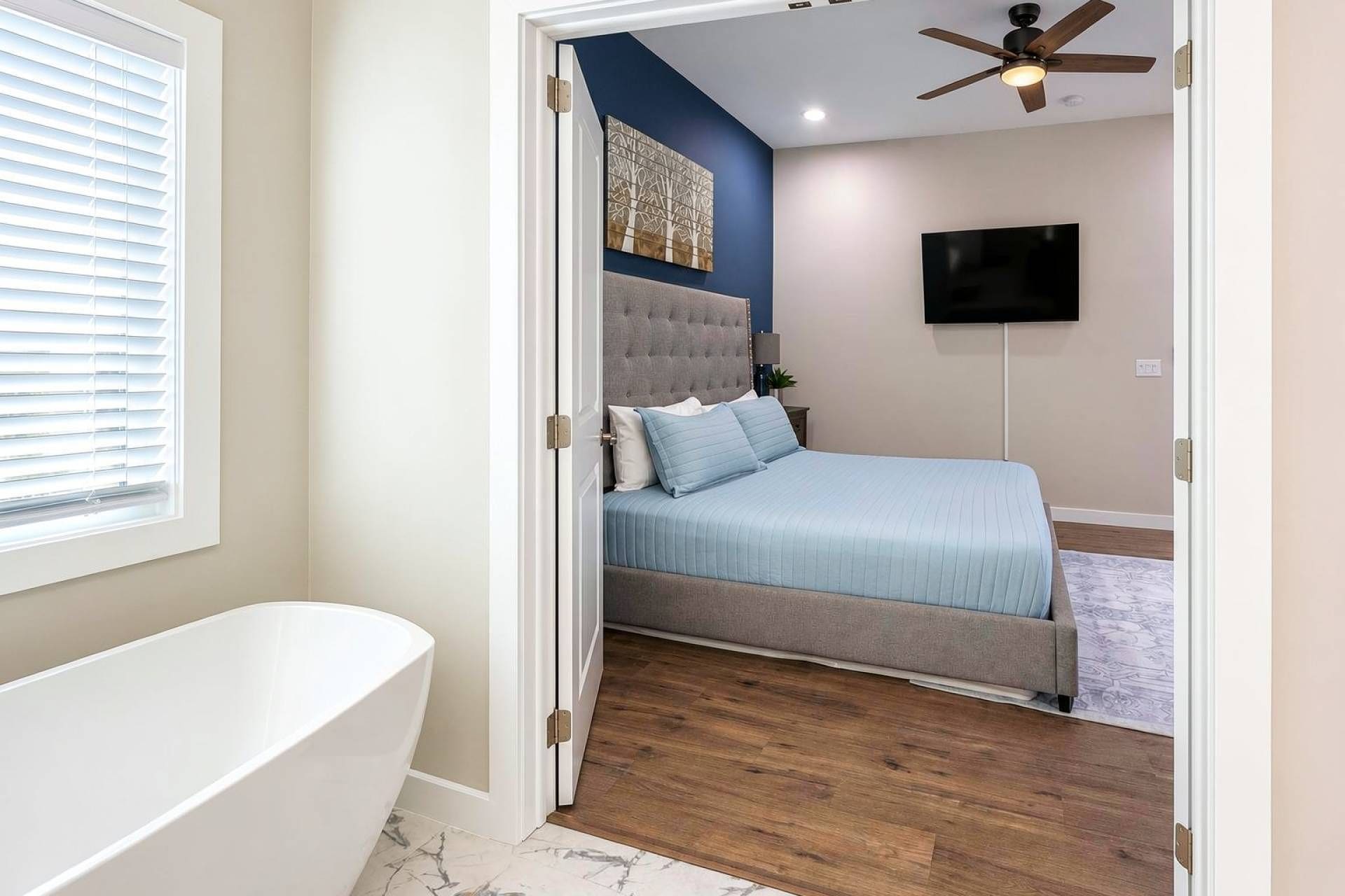 A bedroom with a bed, a TV, a ceiling fan, and a window with blinds.