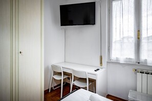 A small, clean room with a white desk, two chairs, a TV mounted on the wall, and a window with curtains. - Rondinella (Florence)