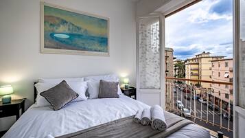 Quarto com cama, almofadas, manta e uma pintura de uma paisagem costeira.