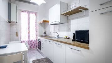 Cocina moderna con armarios blancos, encimera de madera, microondas integrado y un televisor Samsung negro.