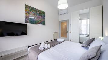 A modern hotel room with a large bed, a flat-screen TV mounted on the wall, a painting above the bed, and a large mirror reflecting the room.