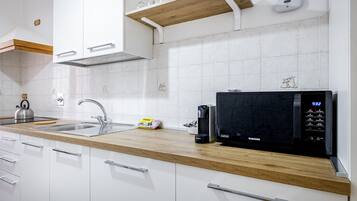 Moderni keittiö, jossa on valkoiset kaapit, puinen työtaso, musta mikroaaltouuni ja vedenkeitin.