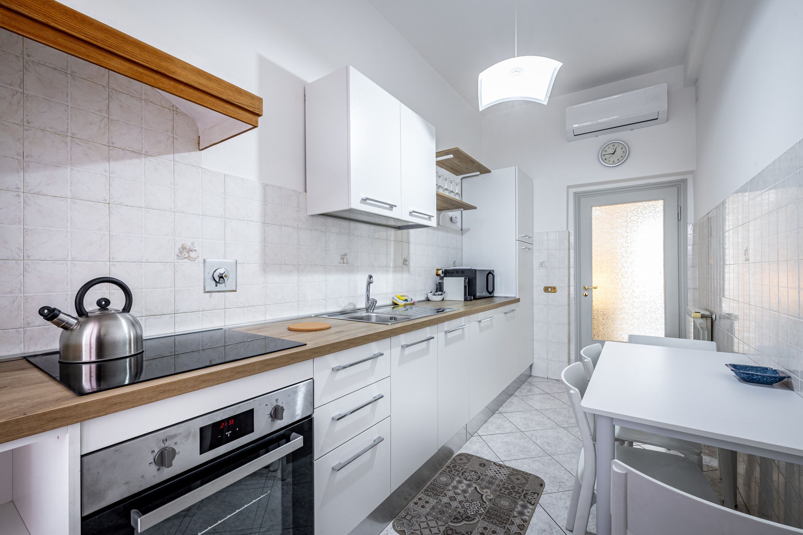 Una cocina moderna con armarios blancos, encimera de madera, horno empotrado y una mesa de comedor con sillas.