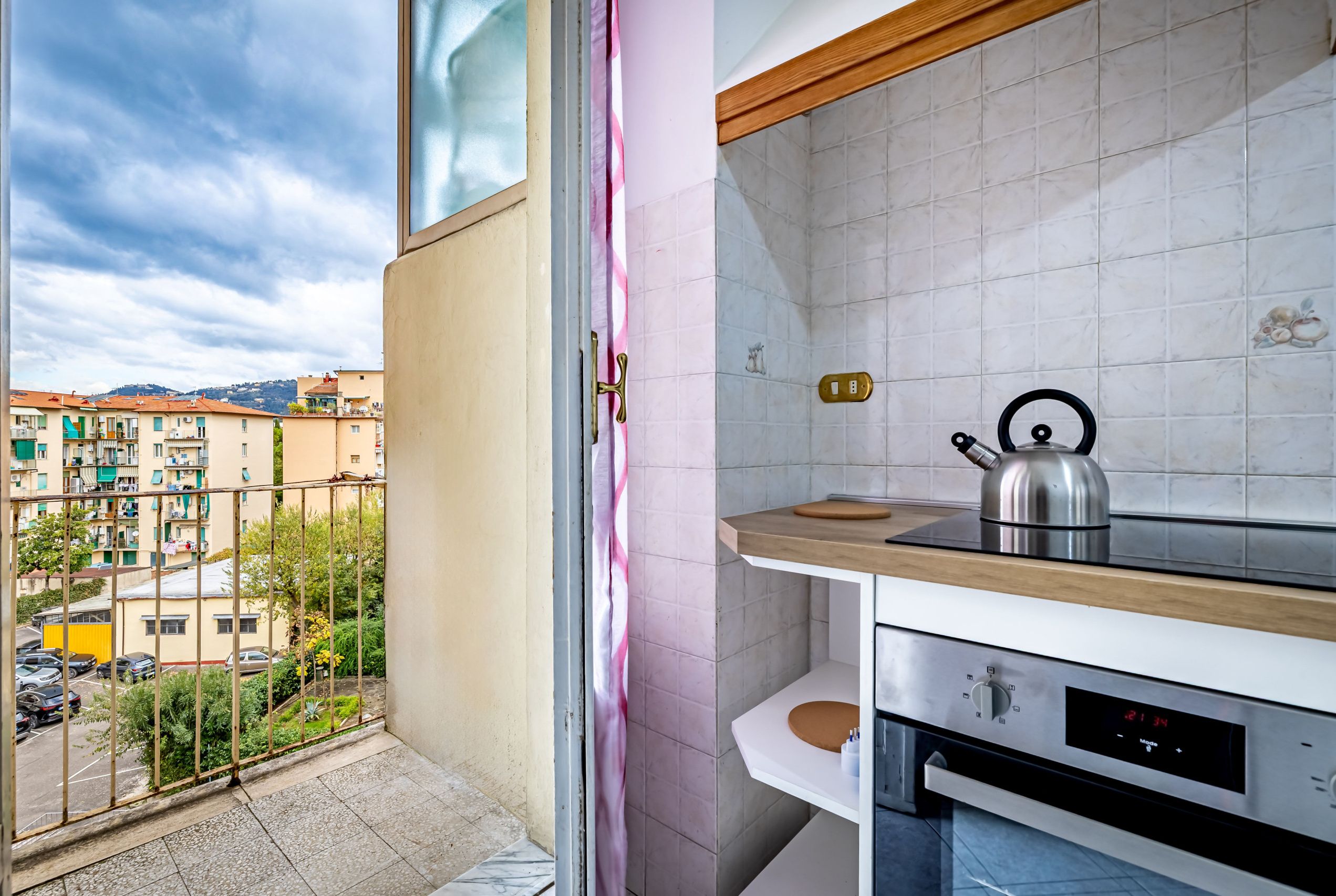 Una cocina con vistas a un balcón, una tetera y un reloj digital.