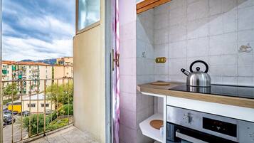 A kitchen with a view of a balcony, a kettle, and a digital clock.