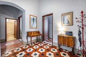 A hallway with a patterned floor, wooden furniture, and framed artwork on the walls. - Mattonaia (Florence)