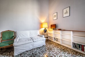A living room with a white sofa, a green chair, a patterned floor, a lamp, and a bookshelf. - Mattonaia (Florence)