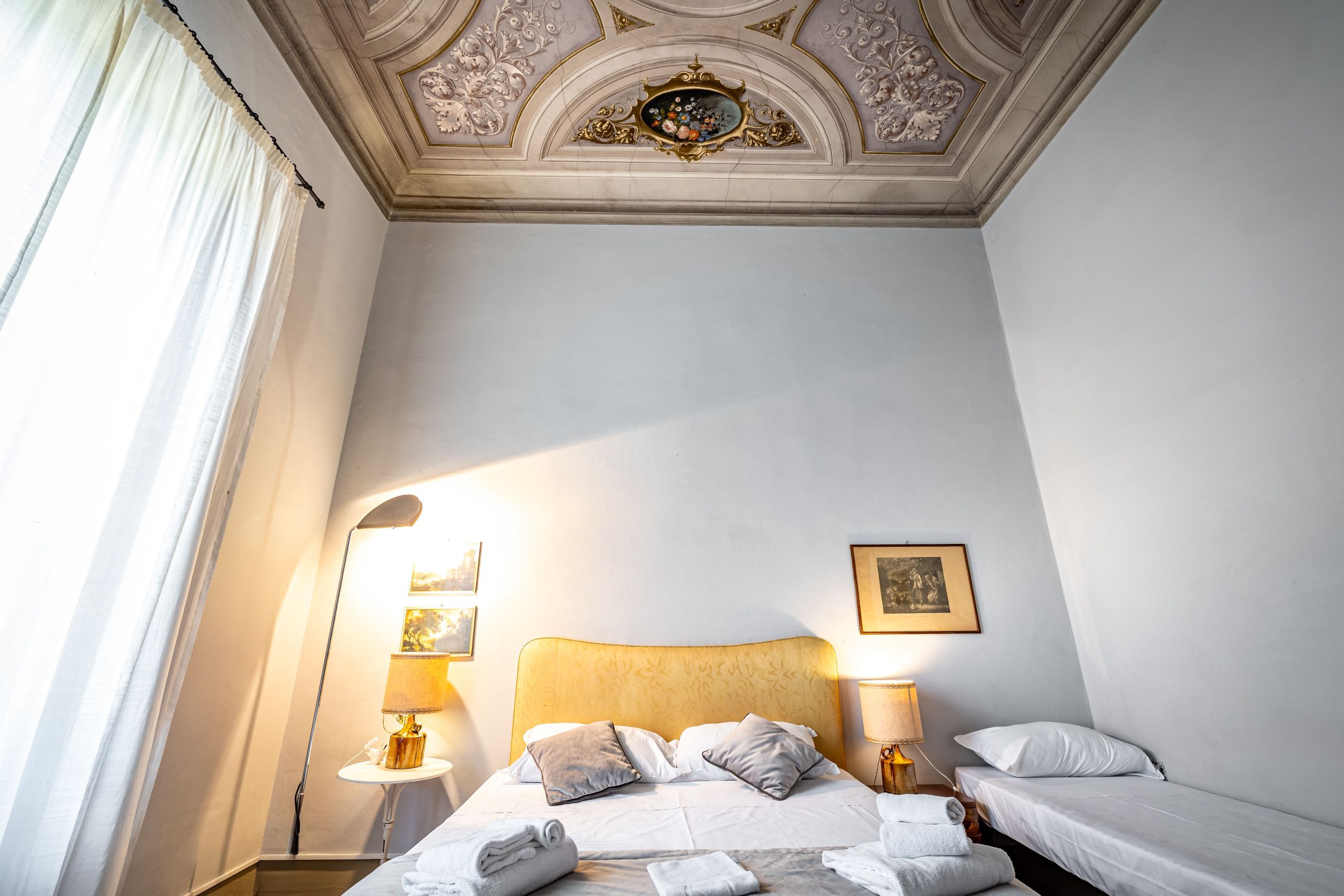 Habitación de hotel con una cama grande, dos mesitas de noche con lámparas, un techo con molduras decorativas y un cuadro en la pared.
