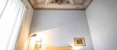Habitación de hotel con una cama grande, dos mesitas de noche con lámparas, un techo con molduras decorativas y un cuadro en la pared.